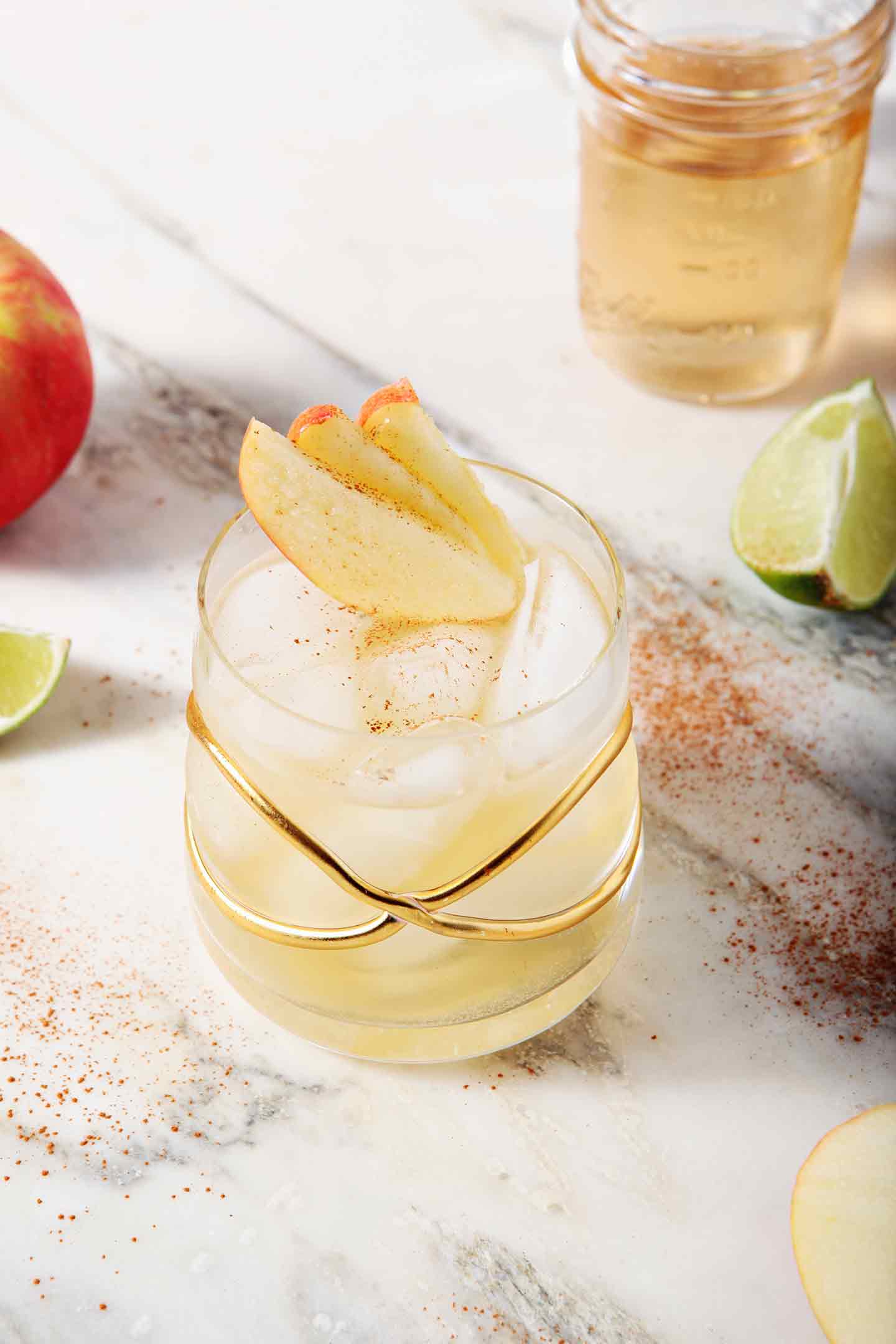 A Apple Pie Moscow Mule sits on a marble background, surrounded by apples and lime slices