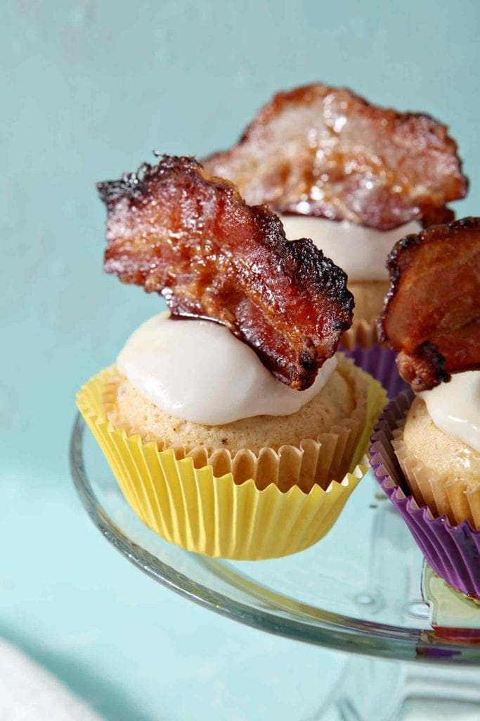 Garnished, complete Bourbon Maple Bacon Cupcakes sit on a cake stand before being eaten