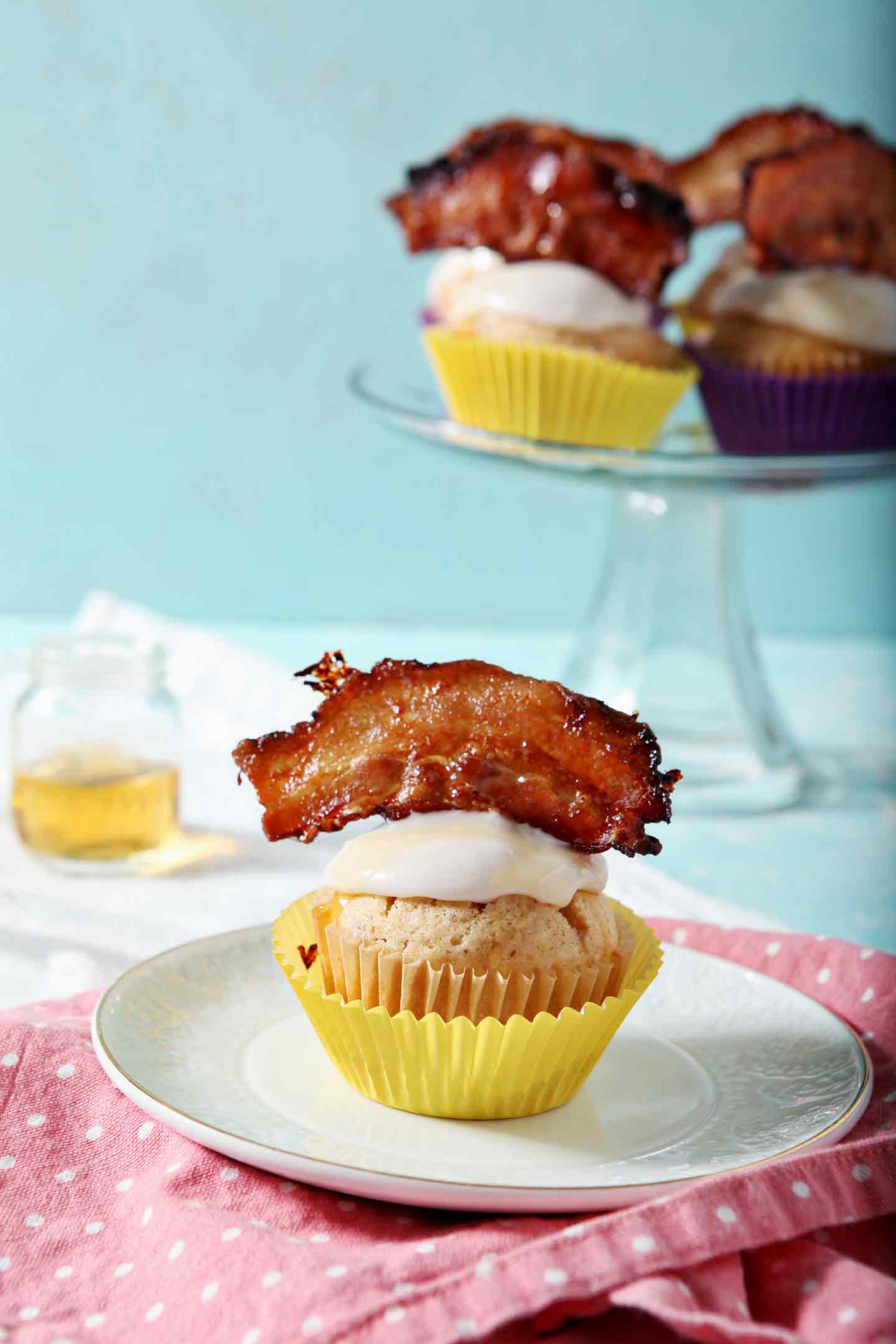 A Bourbon Maple Bacon Cupcake sits on a small plate, garnished with Maple Bacon, and ready for eating