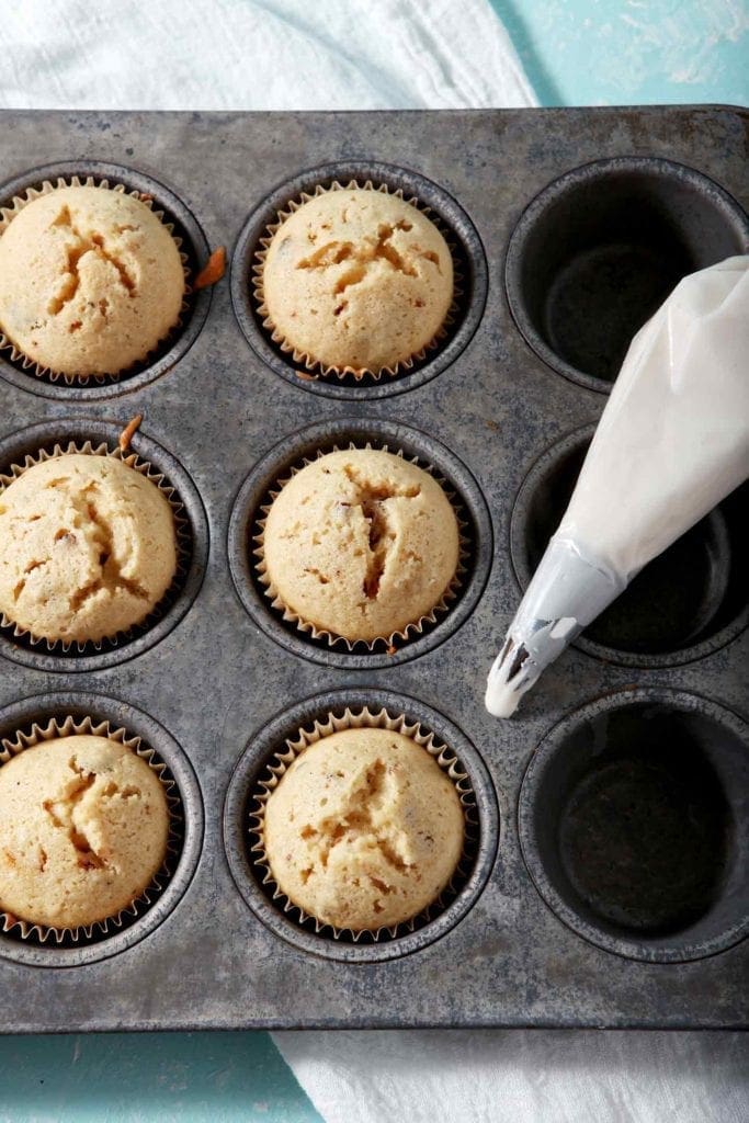 Baked Bourbon Maple Bacon Cupcakes sit in a cupcake tin with a disposable piping bag of Maple Frosting before the cupcakes are frosted