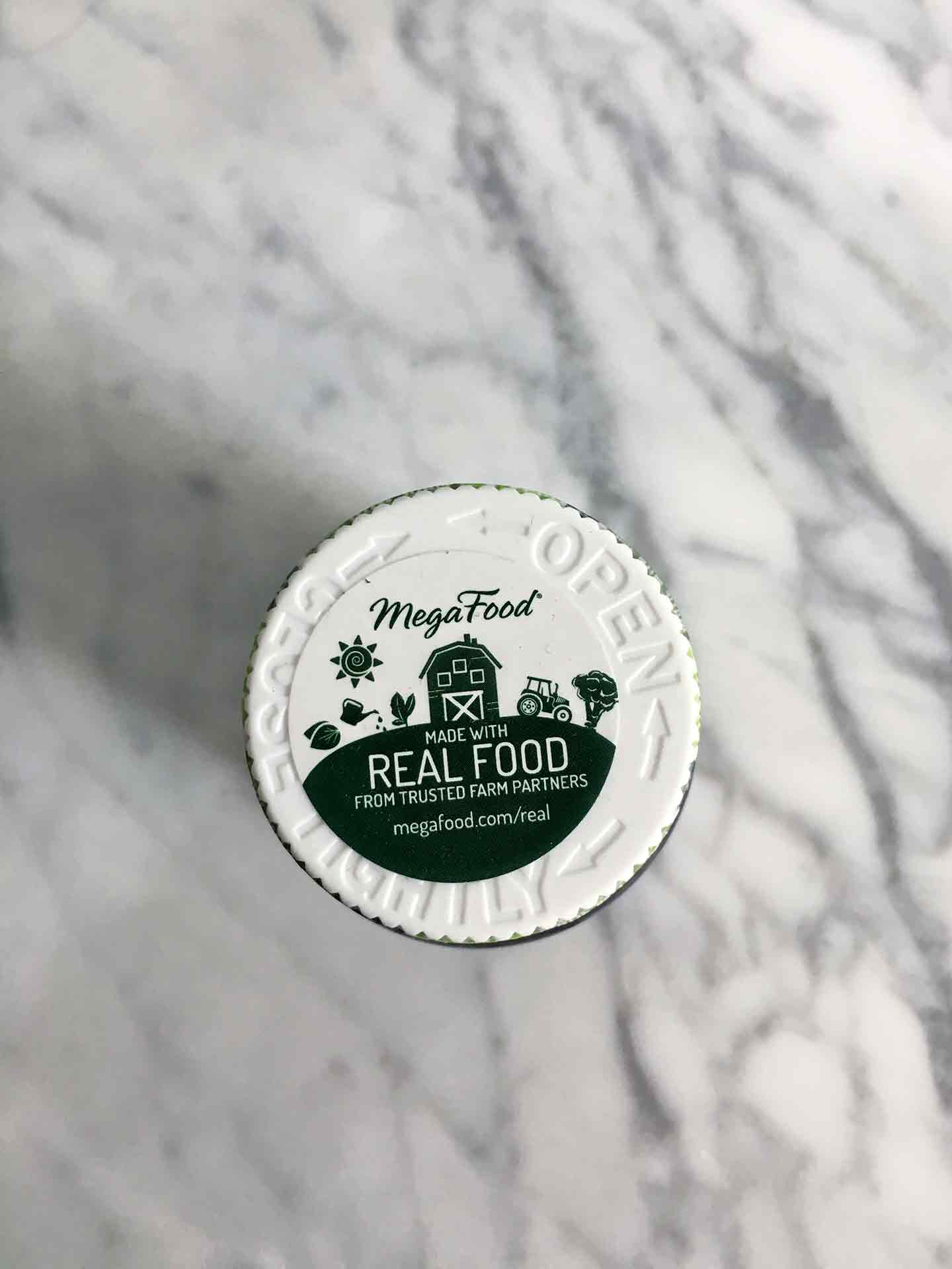 A jar of MegaFood sits on a marble background, touting Real Food ingredients