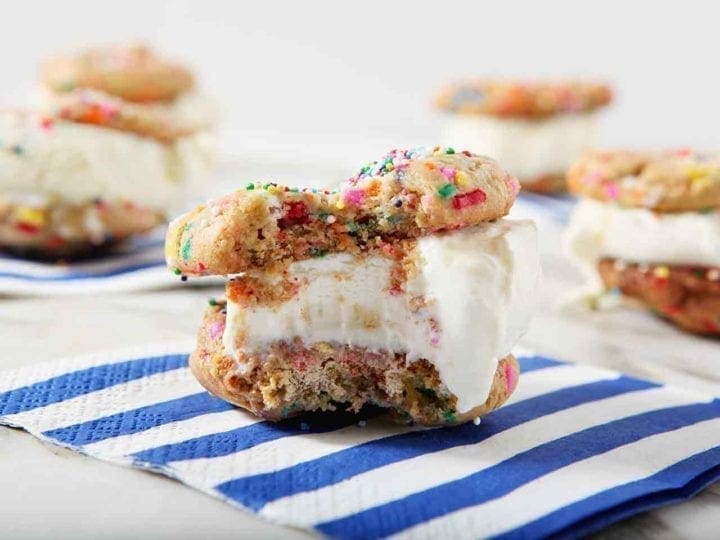 A bitten-into Funfetti Ice Cream Sandwich sits on a blue striped napkin, surrounded by other ice cream sandwiches