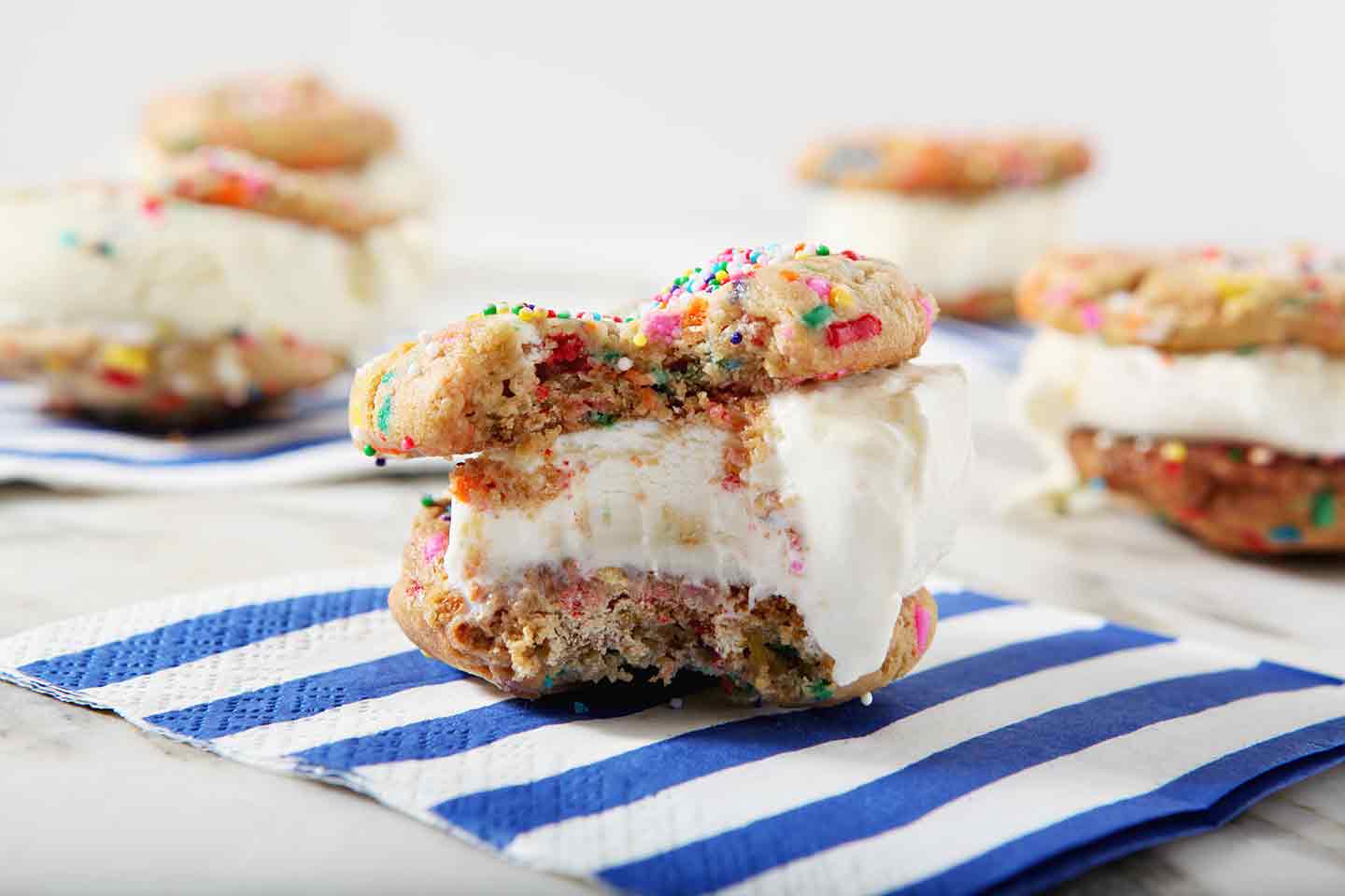 A bitten-into Funfetti Ice Cream Sandwich sits on a blue striped napkin, surrounded by other ice cream sandwiches