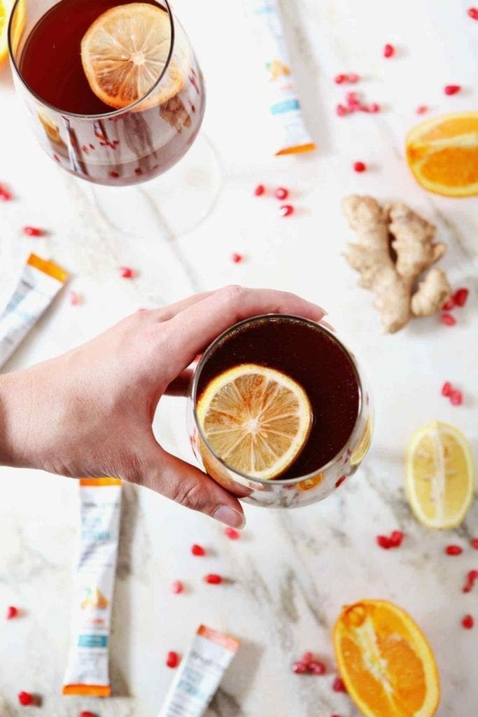 A woman grabs a Pomegranate Ginger Orange Sparkling Mocktail from a marble background