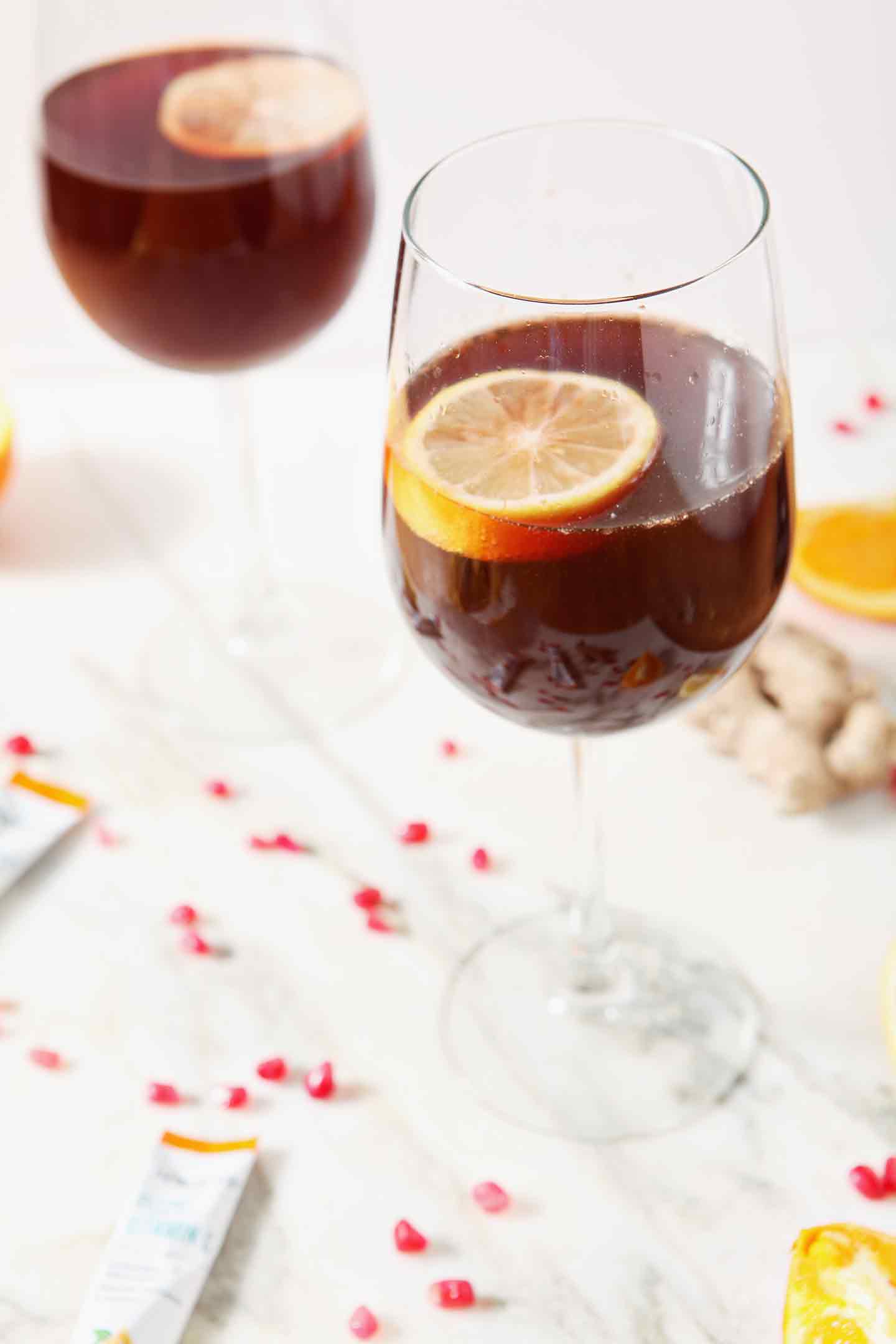 pomegranate ginger orange mocktail in a wine glass with a lemon slice