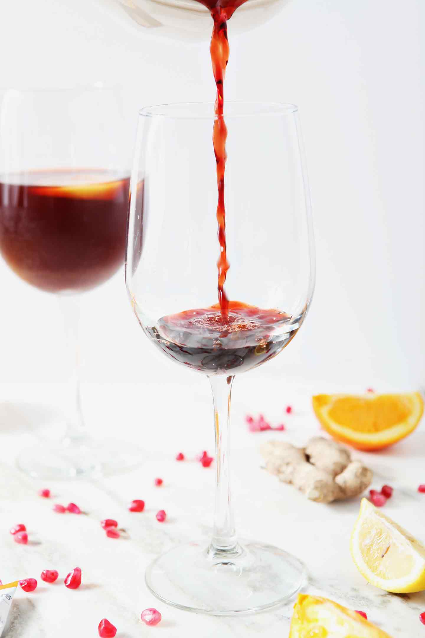 Pomegranate juice is poured into a wine glass to begin making a Pomegranate Ginger Orange Sparkling Mocktail