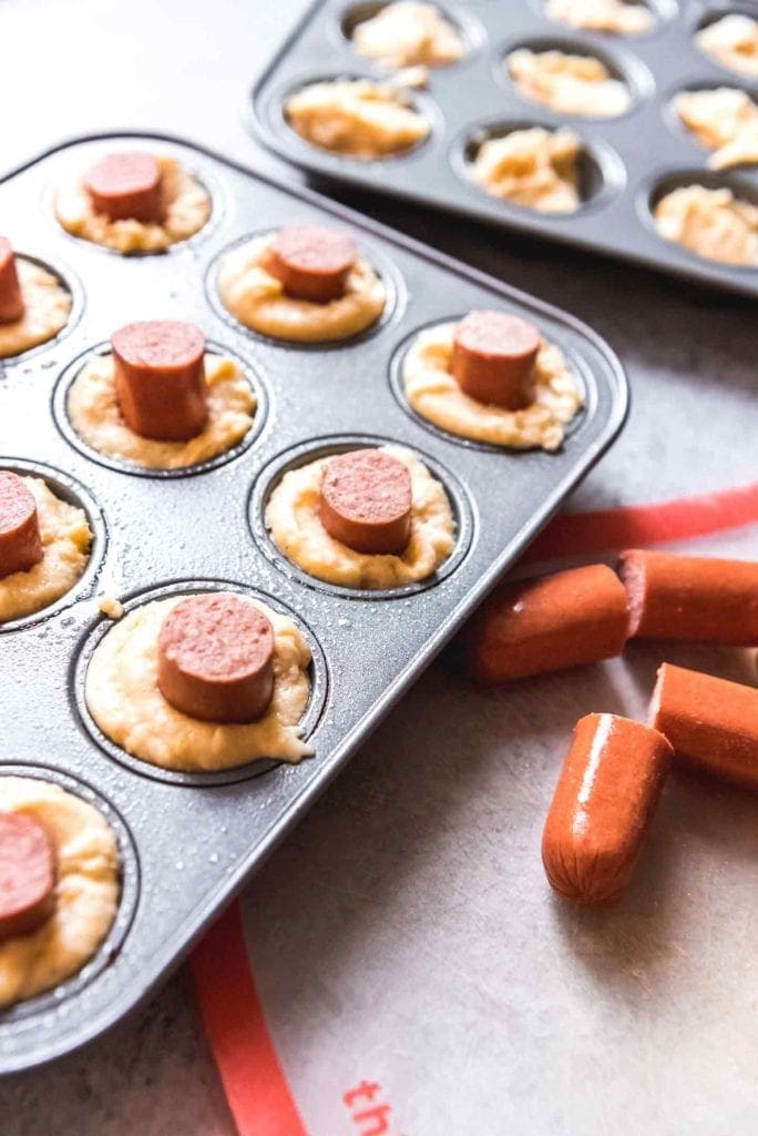 Mini muffins with sliced hot dogs on top of them before baking