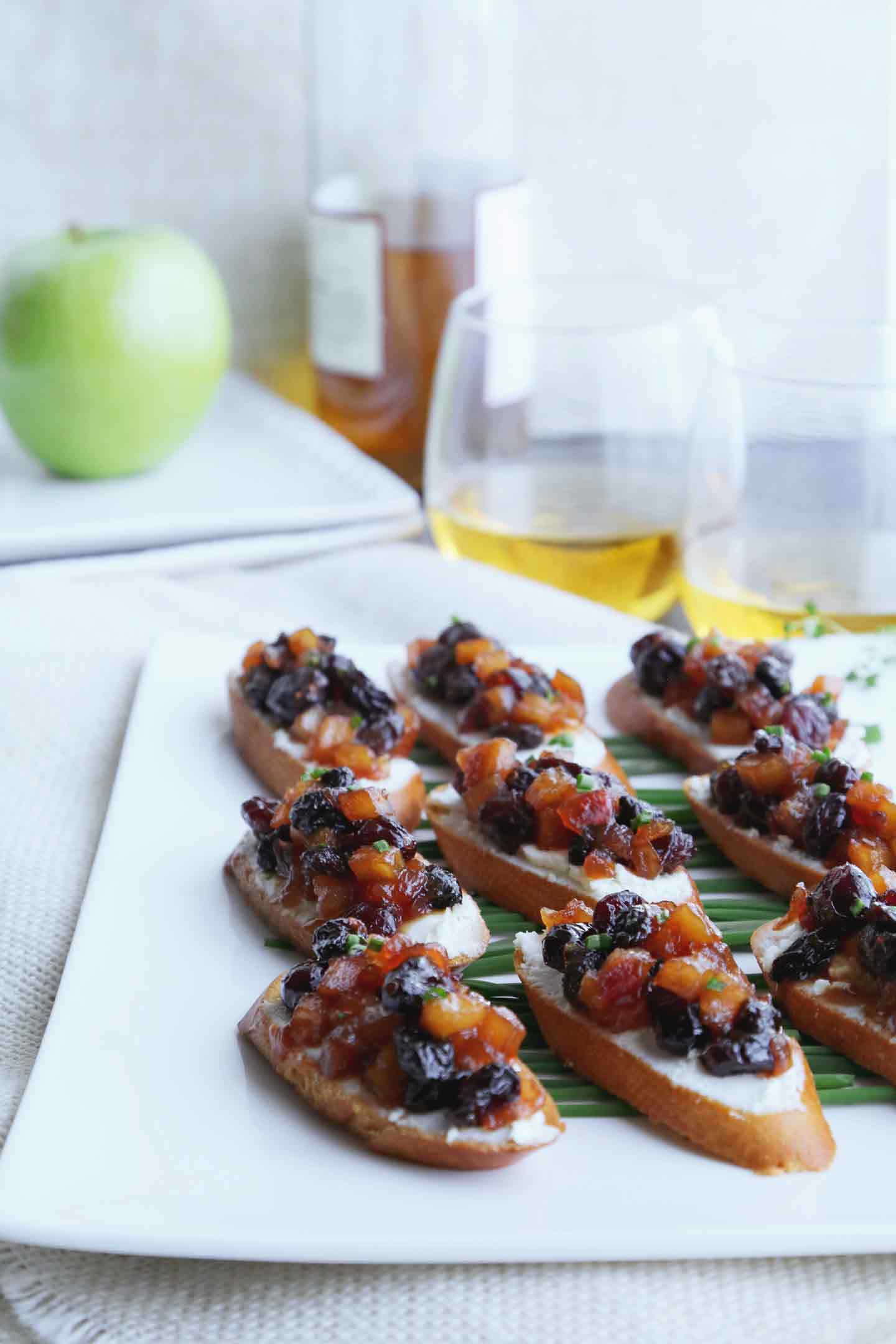 Apple Chutney Bruschetta line a white plate, served with glasses of white wine.