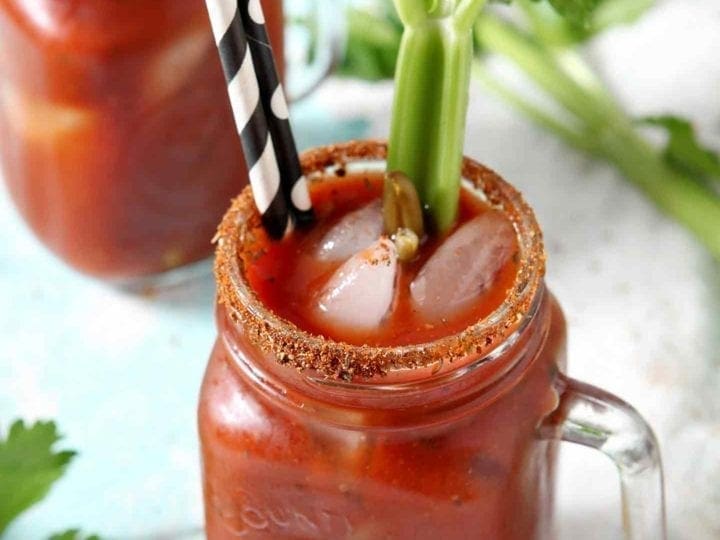 Two BBQ Bloody Marys are garnished with pickled green beans and fresh celery sticks