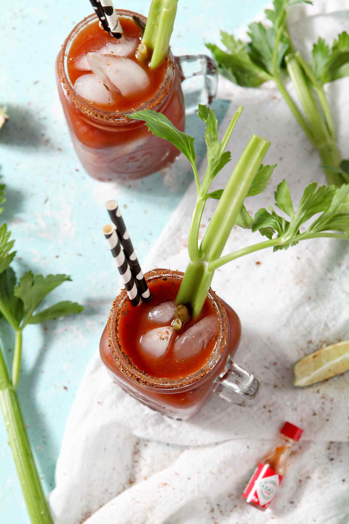 Two BBQ Bloody Mary are seen from above, surrounded by lime slices and celery stalks