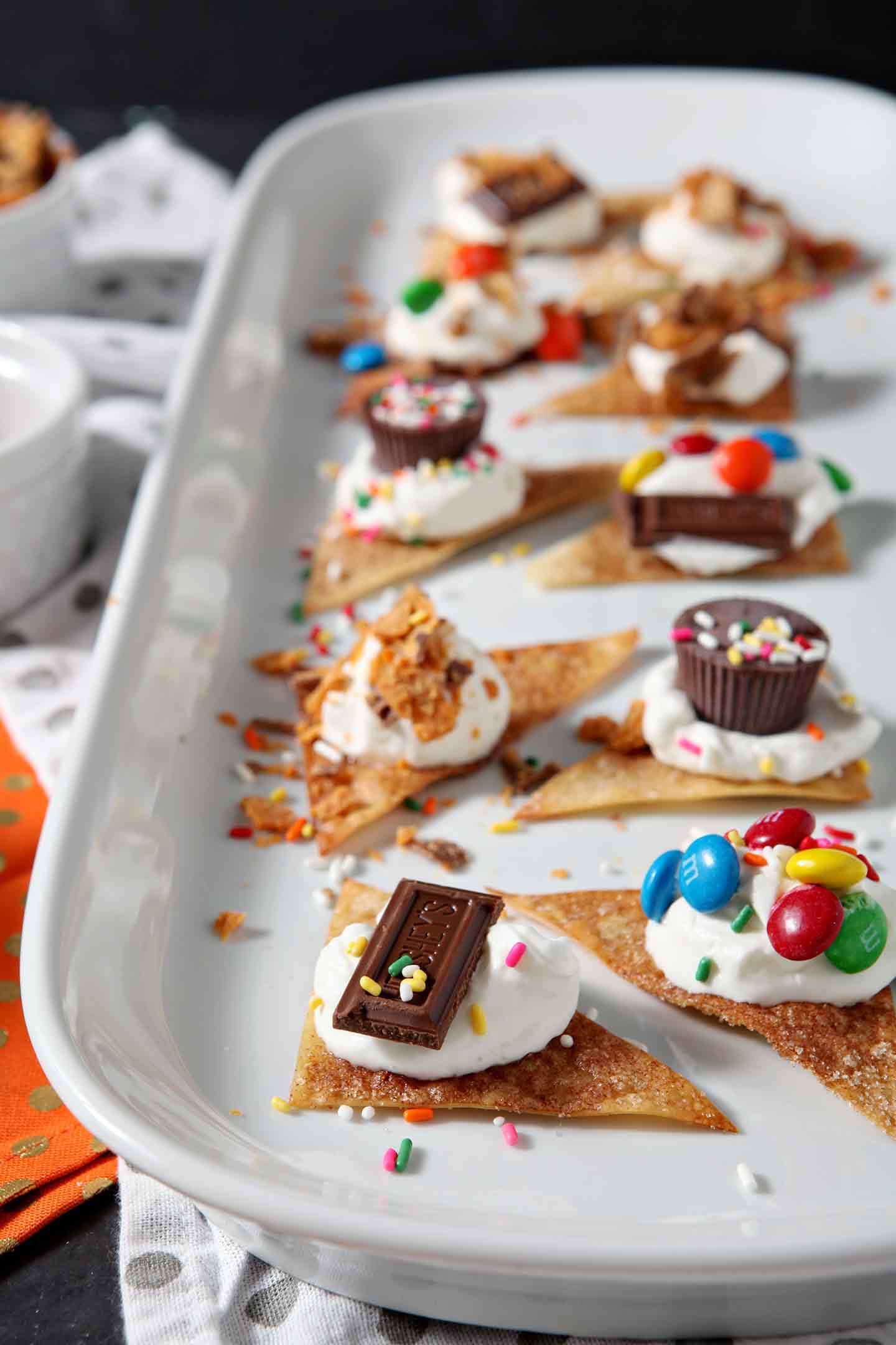 Individual Halloween Dessert Nachos line a long platter, surrounded by additional candy and whipped cream