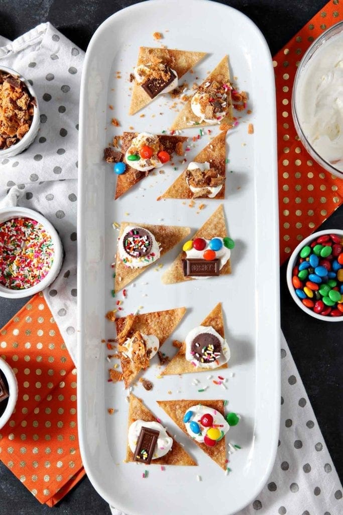 Individually decorated dessert nachos from above on a platter, surrounded by candy