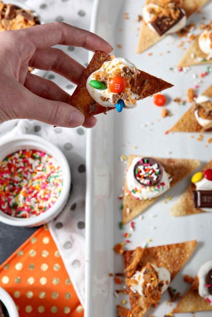 Overhead image of a woman holding a Halloween Dessert Nacho with the platter of the nachos, individually-made, is shown in the background