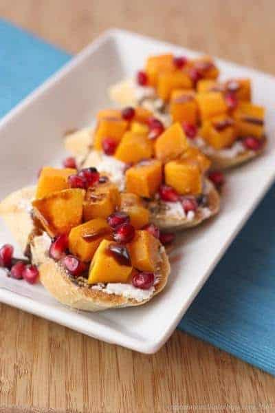 A white platter holds Butternut Squash, Pomegranate and Goat Cheese Crostinis, ready for serving