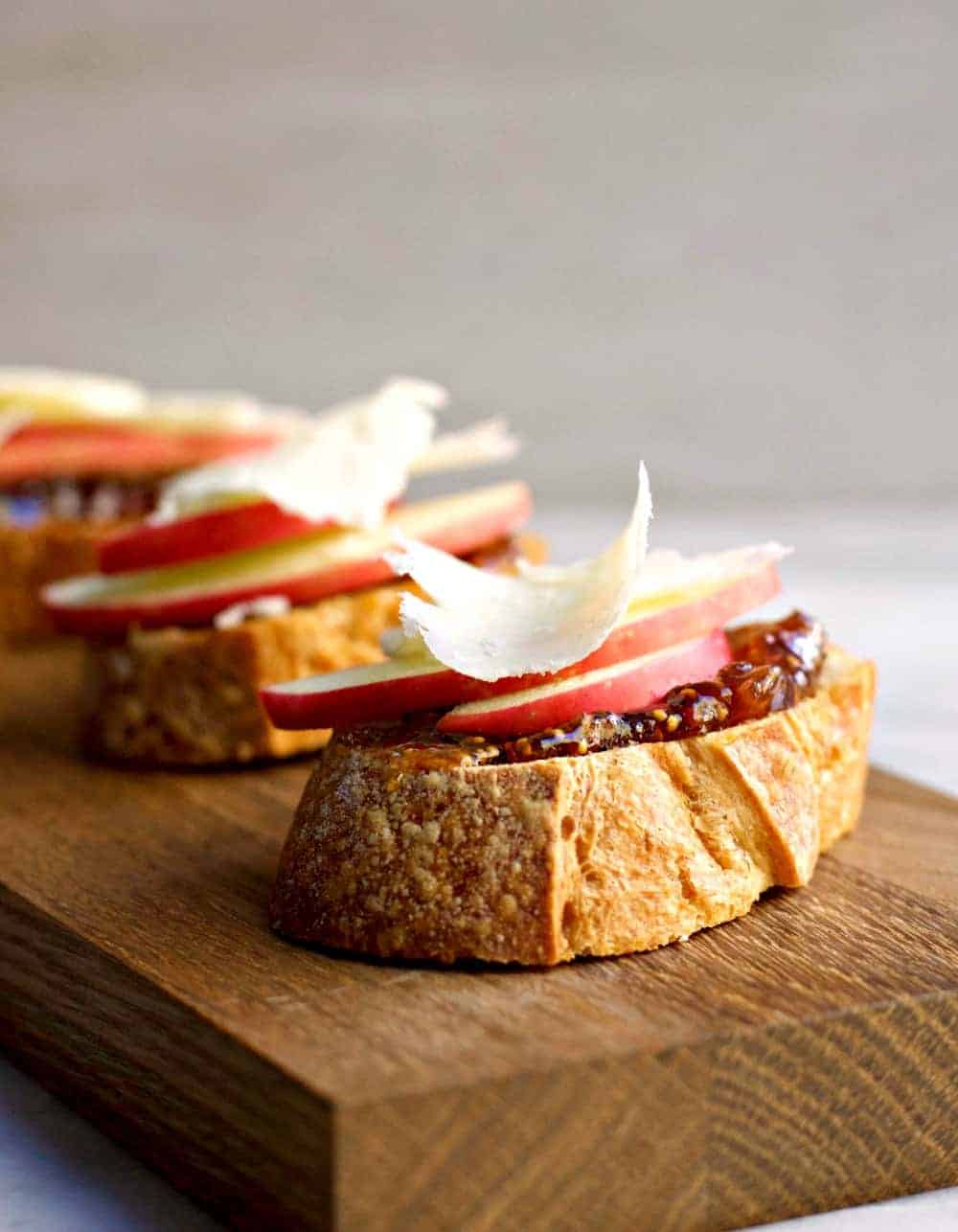 Close up of a few Apple Crostini with Fig Jam and Pecorino sitting on a wooden cutting board