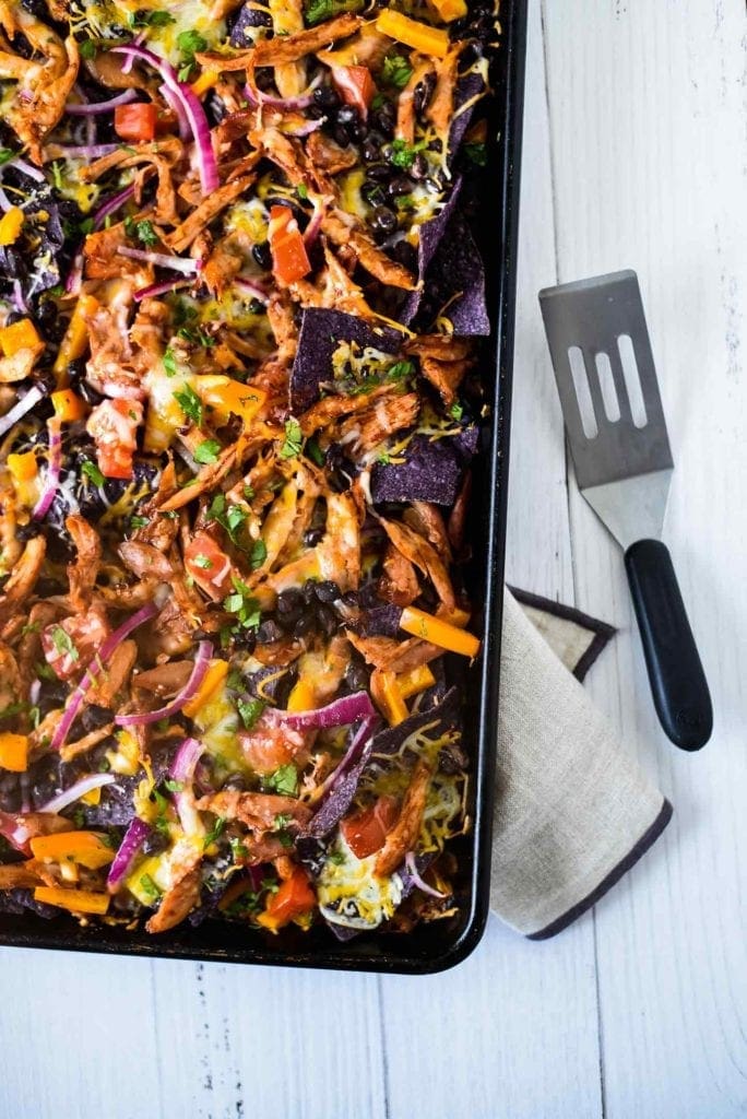 Sheet Pan BBQ Chicken Nachos shown from above on a sheet pan, ready for serving with a spatula