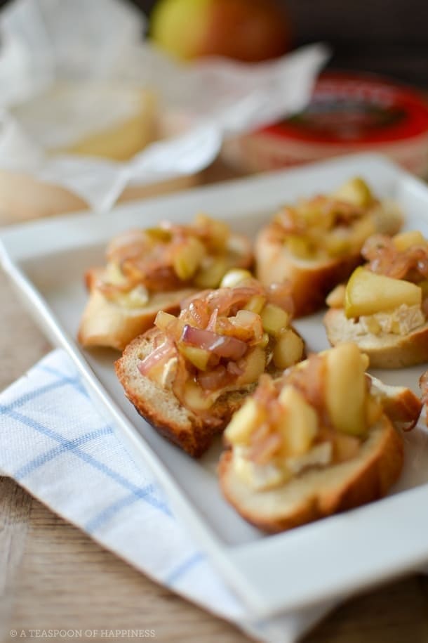 Several Apple and Camembert Crostini with Caramelized Shallots sit on a white tray