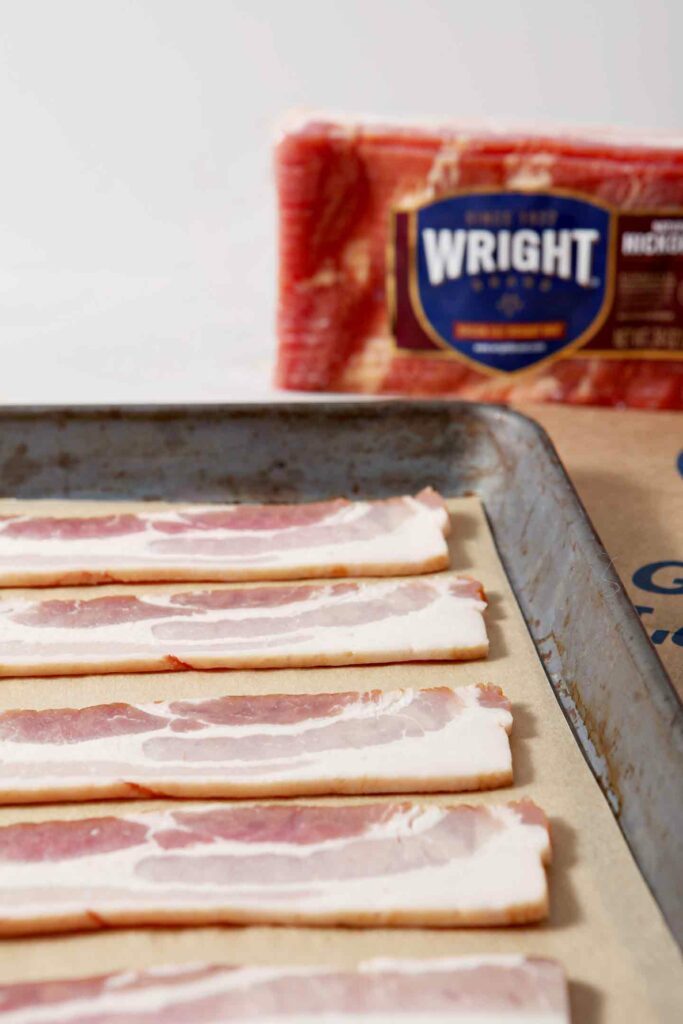 Strips of raw bacon on a baking sheet