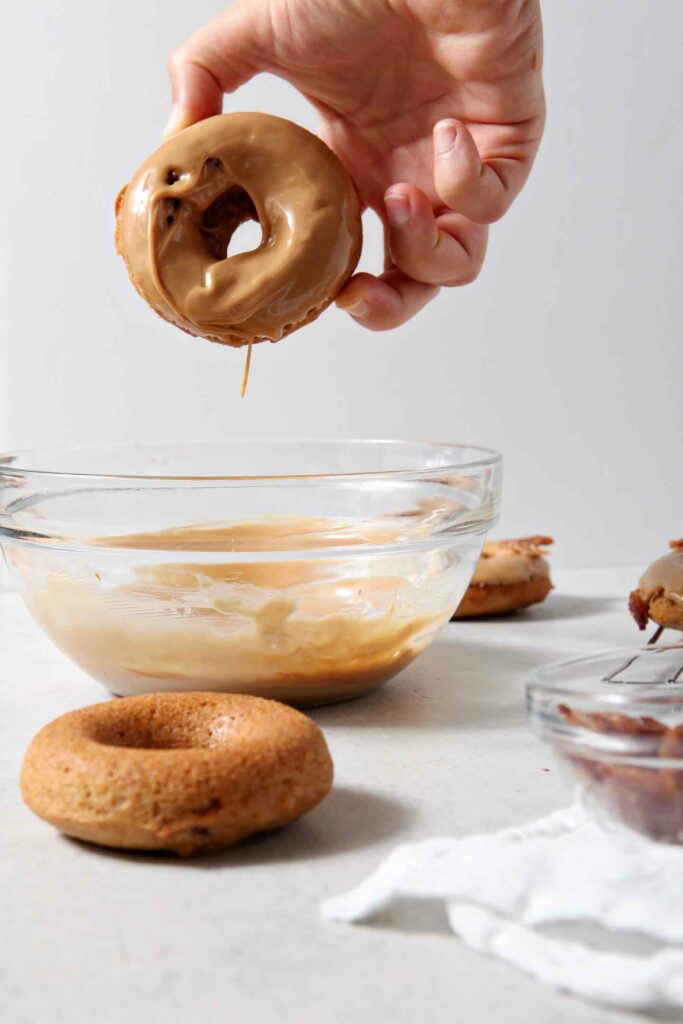 A baked donut is dipped into a maple icing