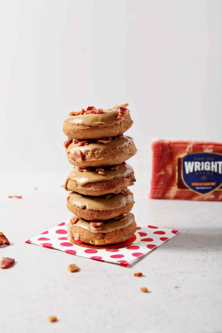 Baked Maple Bacon Donuts are stacked in front of a Wright Brand Bacon package