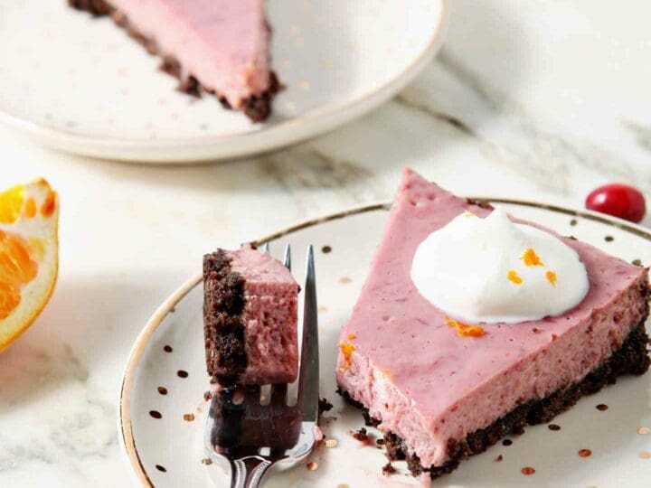 A fork, holding a bite of Creamy Cranberry Tart, sits next to a slice on a gold and white plate