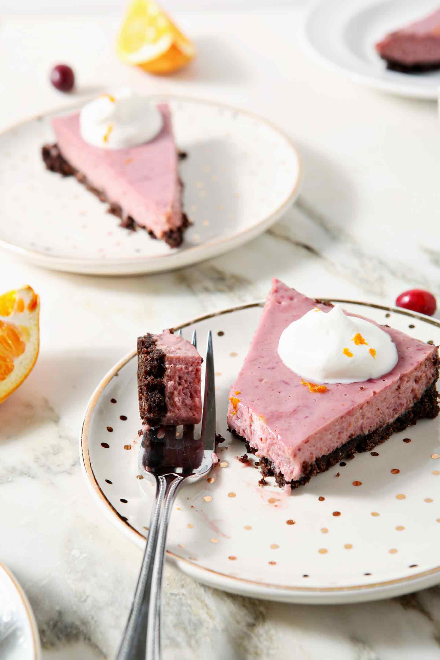 A fork, holding a bite of Creamy Cranberry Tart, sits next to a slice on a gold and white plate