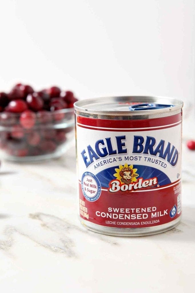 A can of Eagle Brand Sweetened Condensed Milk sits in front of a bowl of fresh cranberries