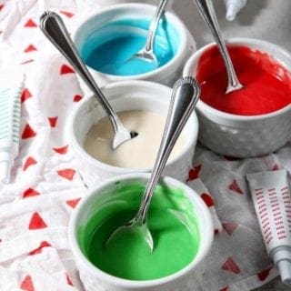 Five white ramekins hold different colors of Easy Sugar Cookie Icing, ready for decorating