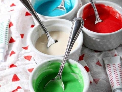 Five white ramekins hold different colors of Easy Sugar Cookie Icing, ready for decorating