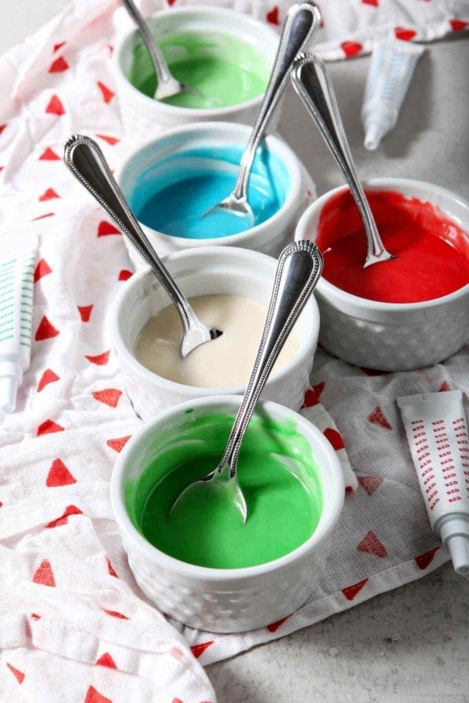 Five white ramekins hold different colors of Easy Sugar Cookie Icing, ready for decorating