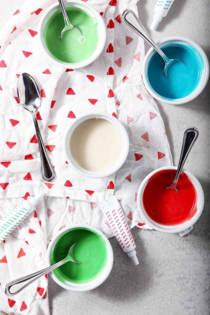 Colored Easy Sugar Cookie Icing is shown in five different ramekins, showing off different colors, before decorating cookies