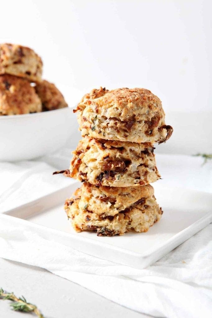 Freshly baked French Onion Biscuits are stacked on top of each other on a plate with a bowl of them in the background