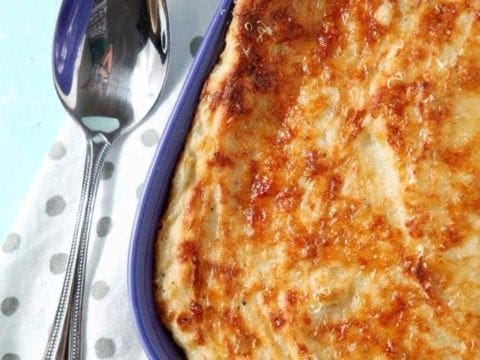 A close up of Garlic Parmesan Mashed Potato Casserole, shown in a purple baking dish with a serving spoon