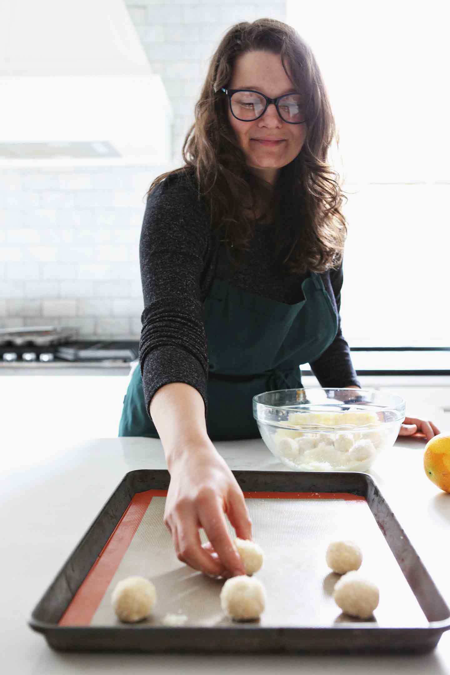 A woman places cookies coated in orange sugar on a baking sheet