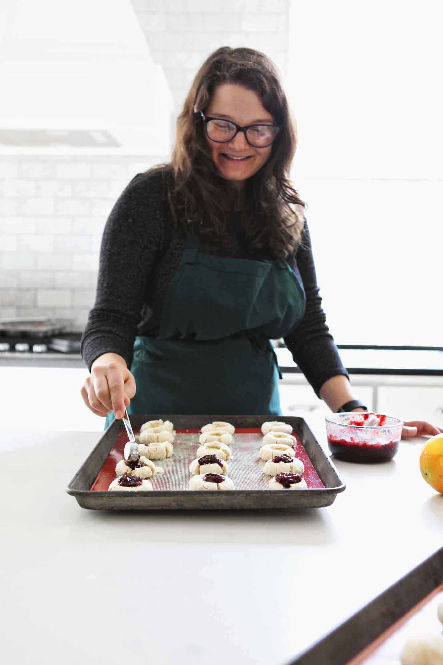 A woman dollops cranberry sauce into the thumbprint cookies