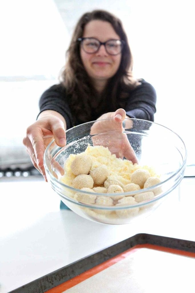 A woman holds a bowl containing orange sugar and cookie dough