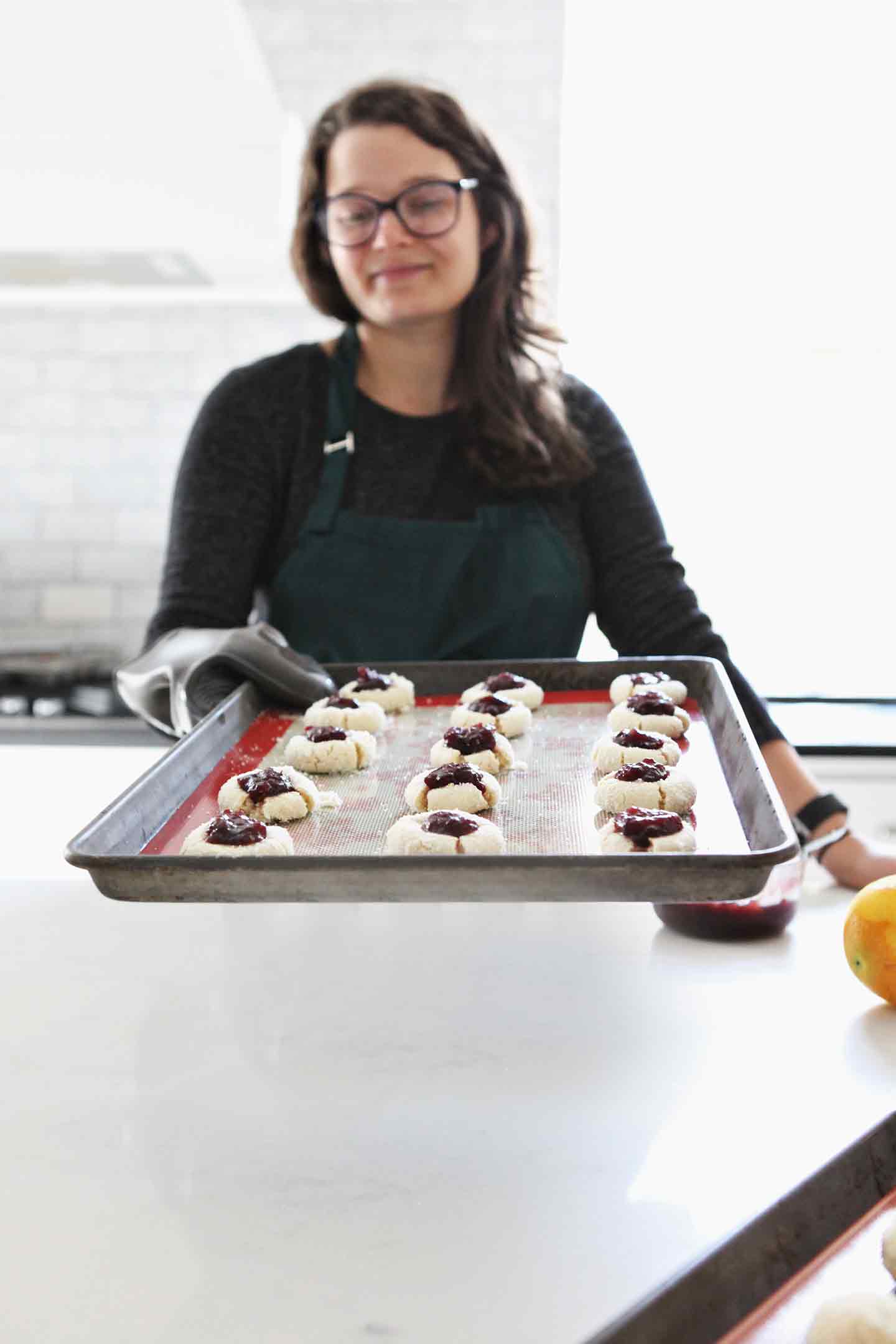 A woman holds a tray of thumbprint cookies toward the camera