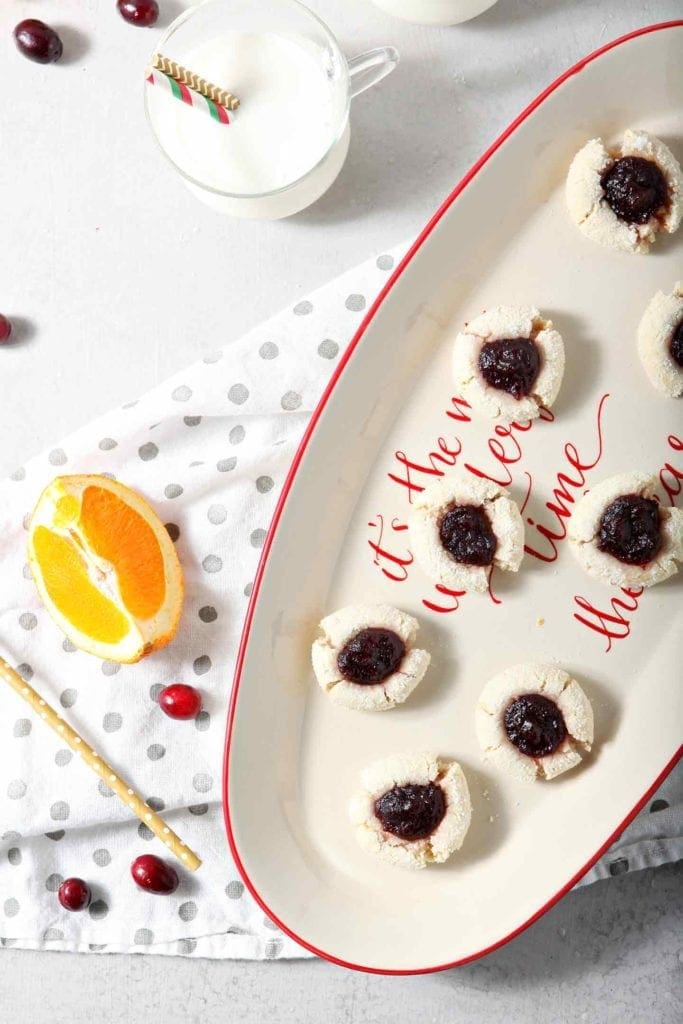 Orange Cranberry Cream Cheese Thumbprint Cookies are served on an oval serving tray with glasses of milk, shown from above