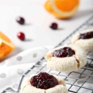 Orange Cranberry Cream Cheese Thumbprint Cookies cool on a wire cooling rack, surrounded by fresh cranberries and orange slices