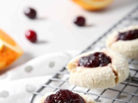 Orange Cranberry Cream Cheese Thumbprint Cookies cool on a wire cooling rack, surrounded by fresh cranberries and orange slices