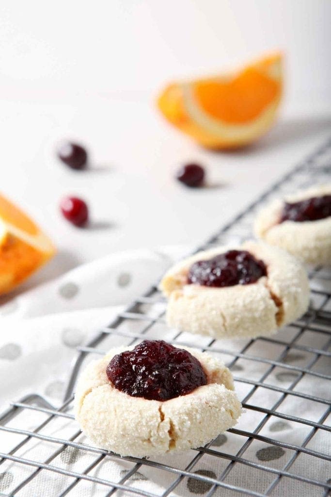 Orange Cranberry Cream Cheese Thumbprint Cookies cool on a wire cooling rack, surrounded by fresh cranberries and orange slices