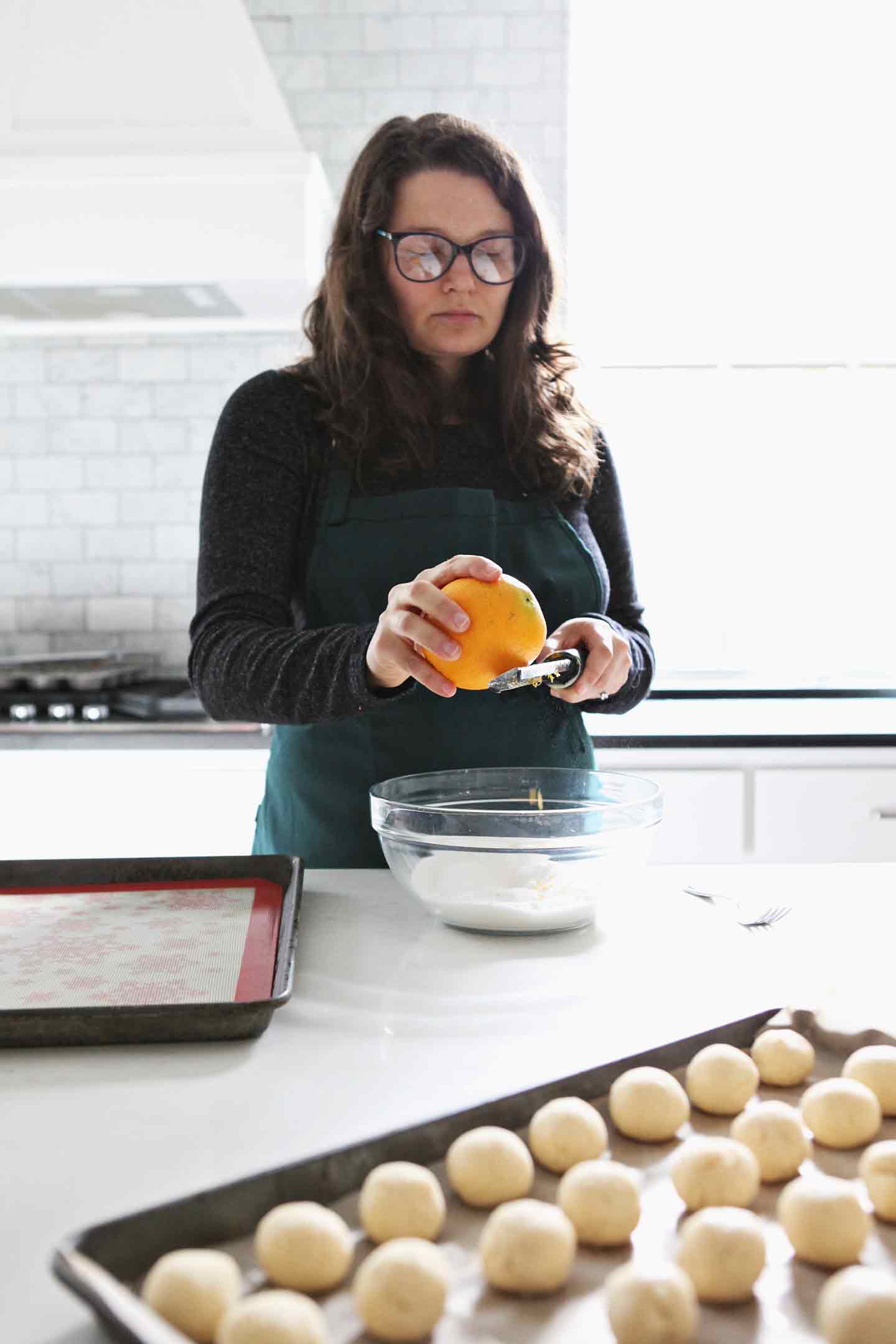 A woman zests an orange into sugar to roll the cookies in