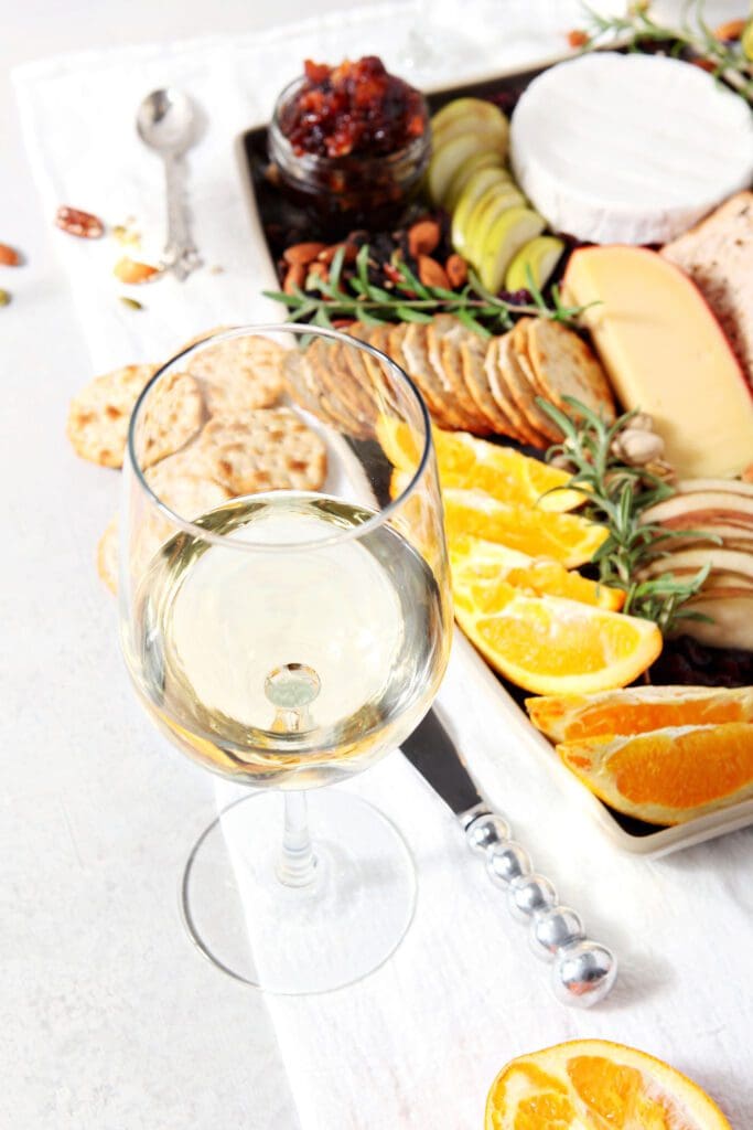 a glass of white wine sits next to a thanksgiving cheese platter