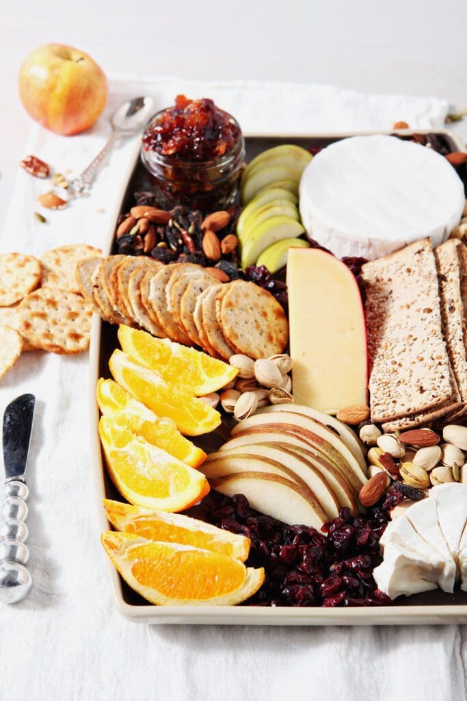 orange slices and other fresh fruit sit on a cheese board for thanksgiving on a grey backdrop