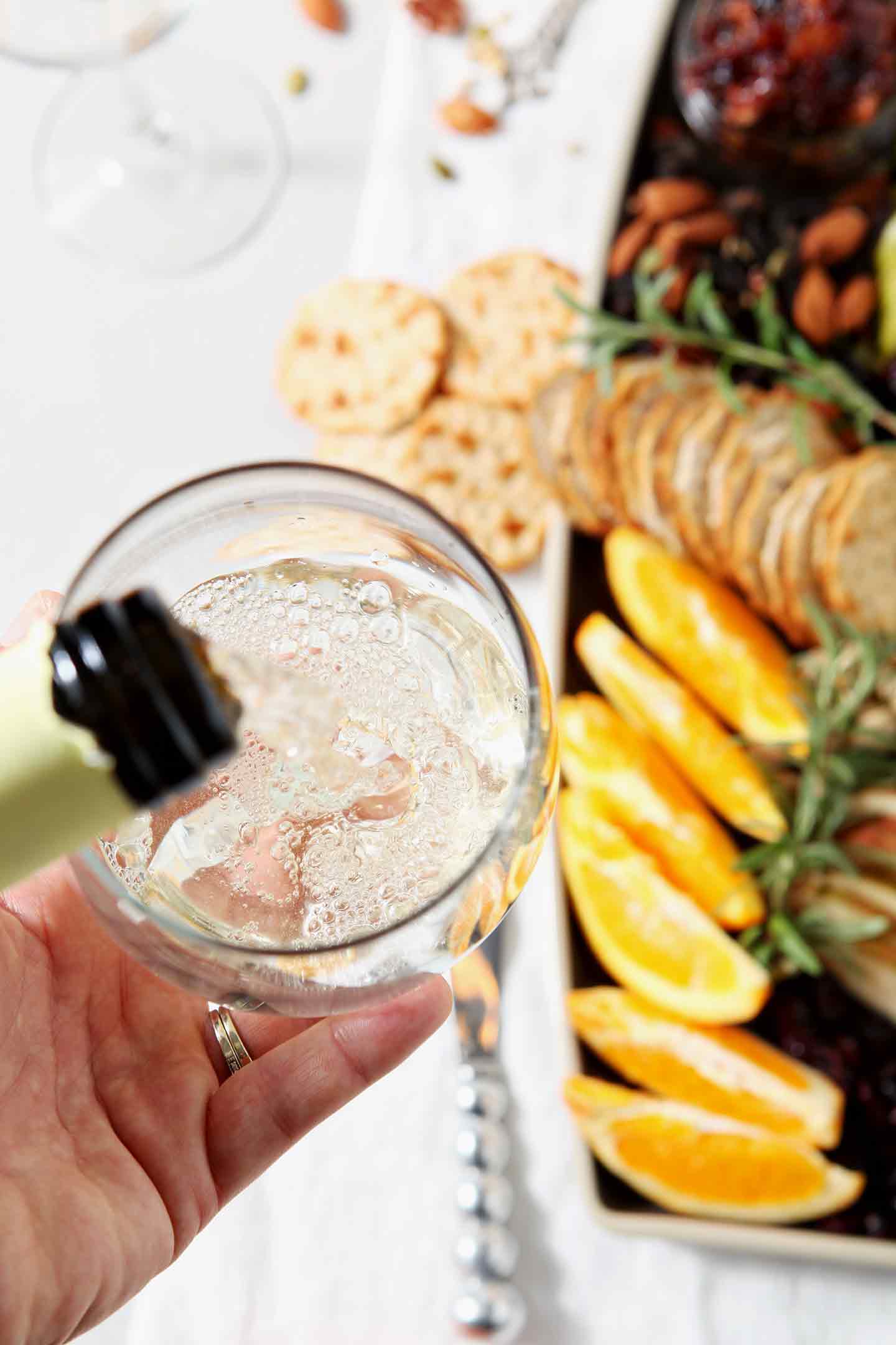 A person pours Vinho Verde wine into a glass next to a Thanksgiving Cheese Board.