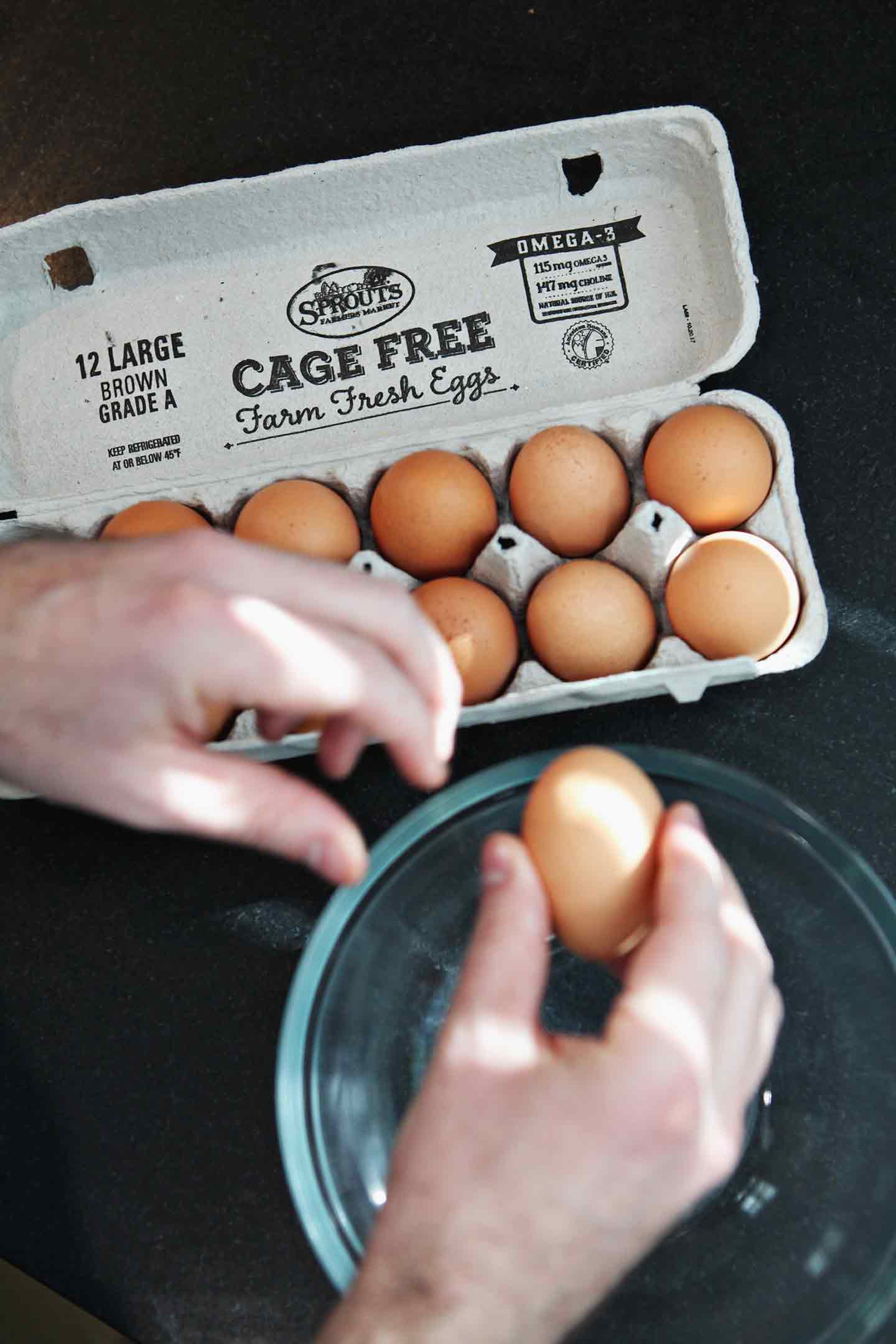 A man breaks eggs into a large glass bowl before making scrambled eggs