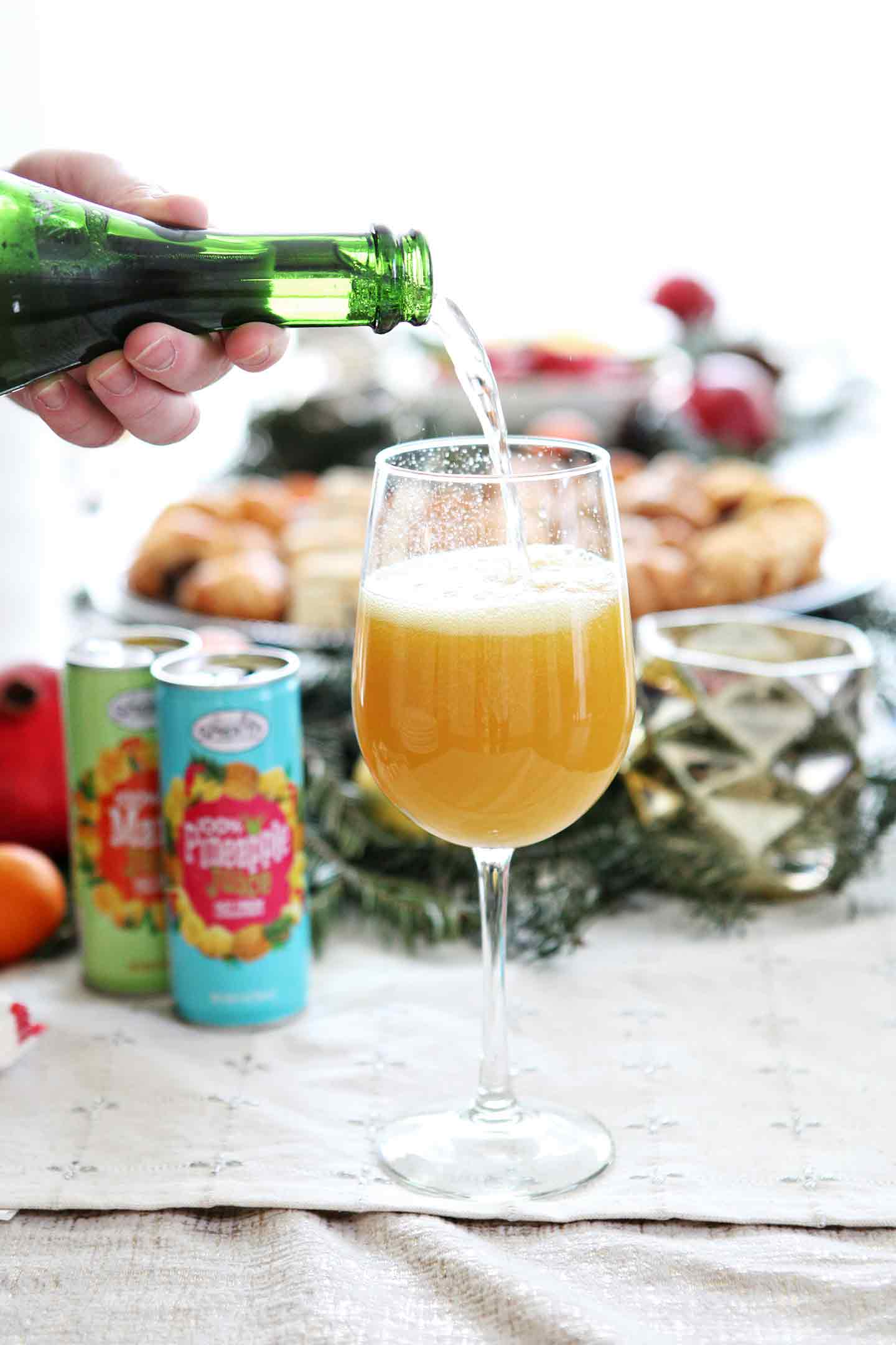 Champagne is poured into a wine glass with mango juice to make a tropical mimosa