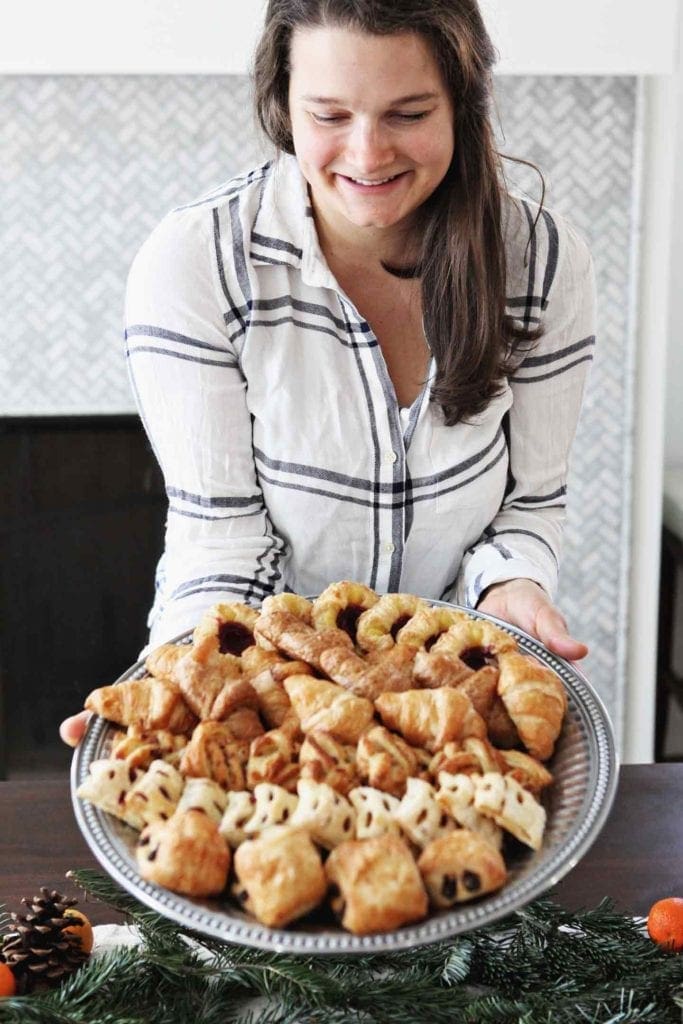 A woman holds a tray holding European-style pastries for a brunch table