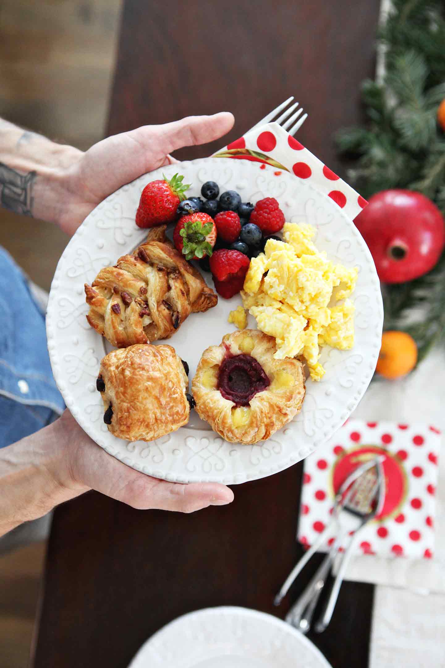 A man holds a white plate holding various dishes from a holiday brunch