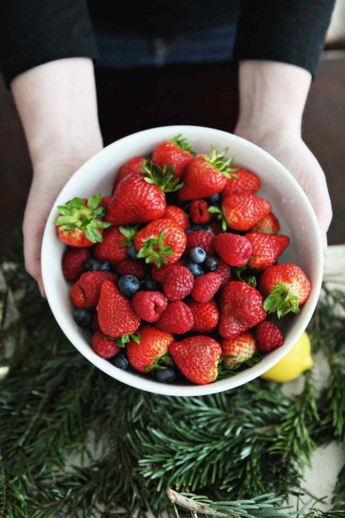 A woman holds a bowl of fresh berries over a holiday brunch tablescape